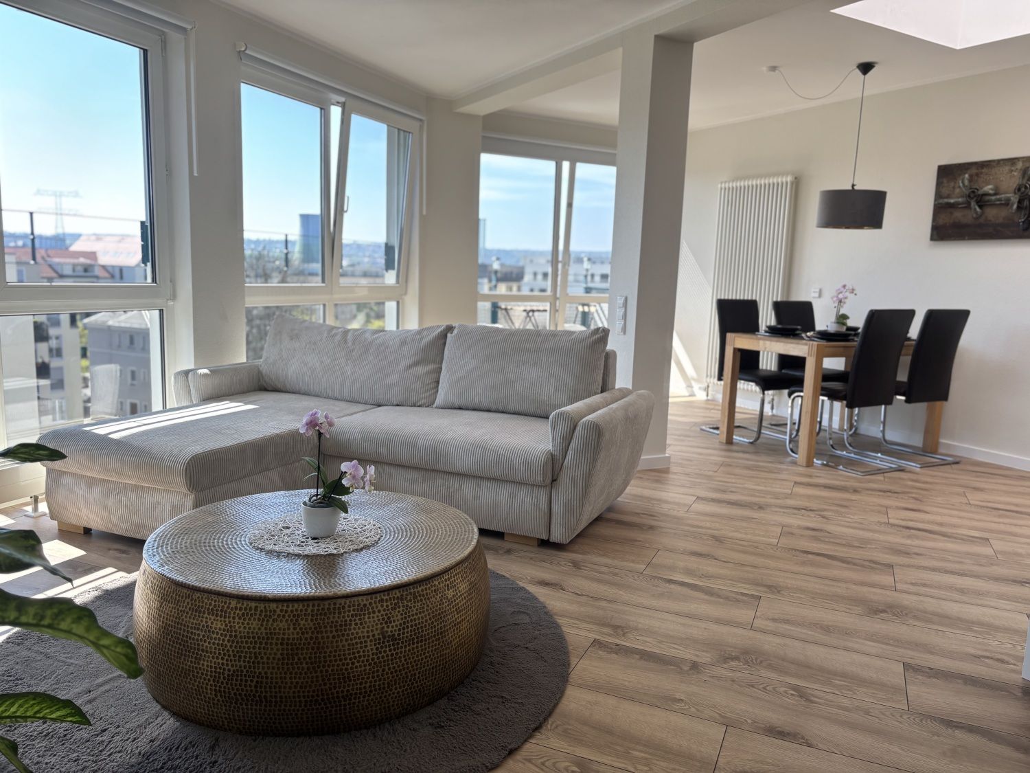 Wohnzimmer mit hellem Ecksofa, goldenem Couchtisch und Panoramafenstern über die Dächer von Dresden