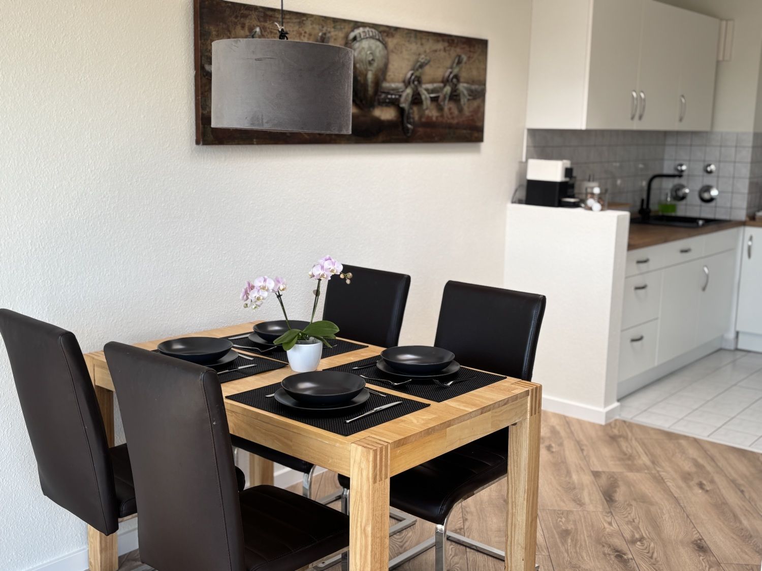 Gedeckter Esstisch aus Holz mit vier Stühlen vor der offenen Küche