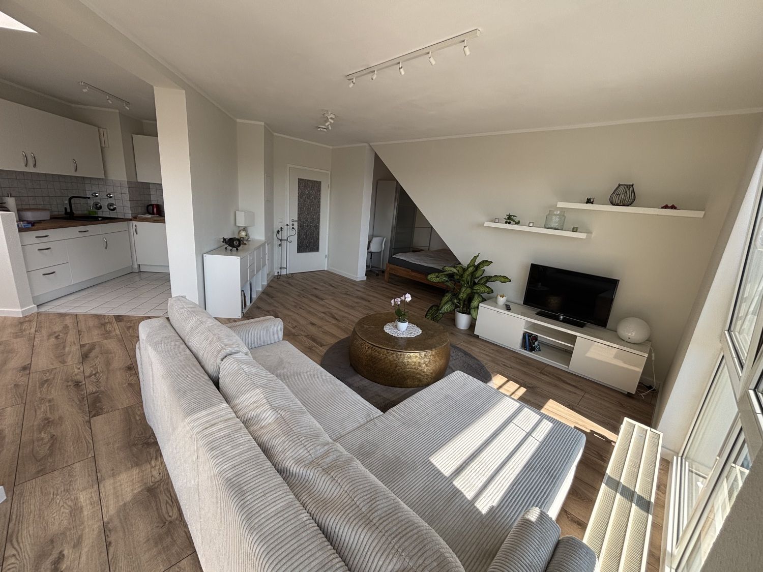 Wohnraum mit Ecksofa, Fernseher und angrenzender Küche