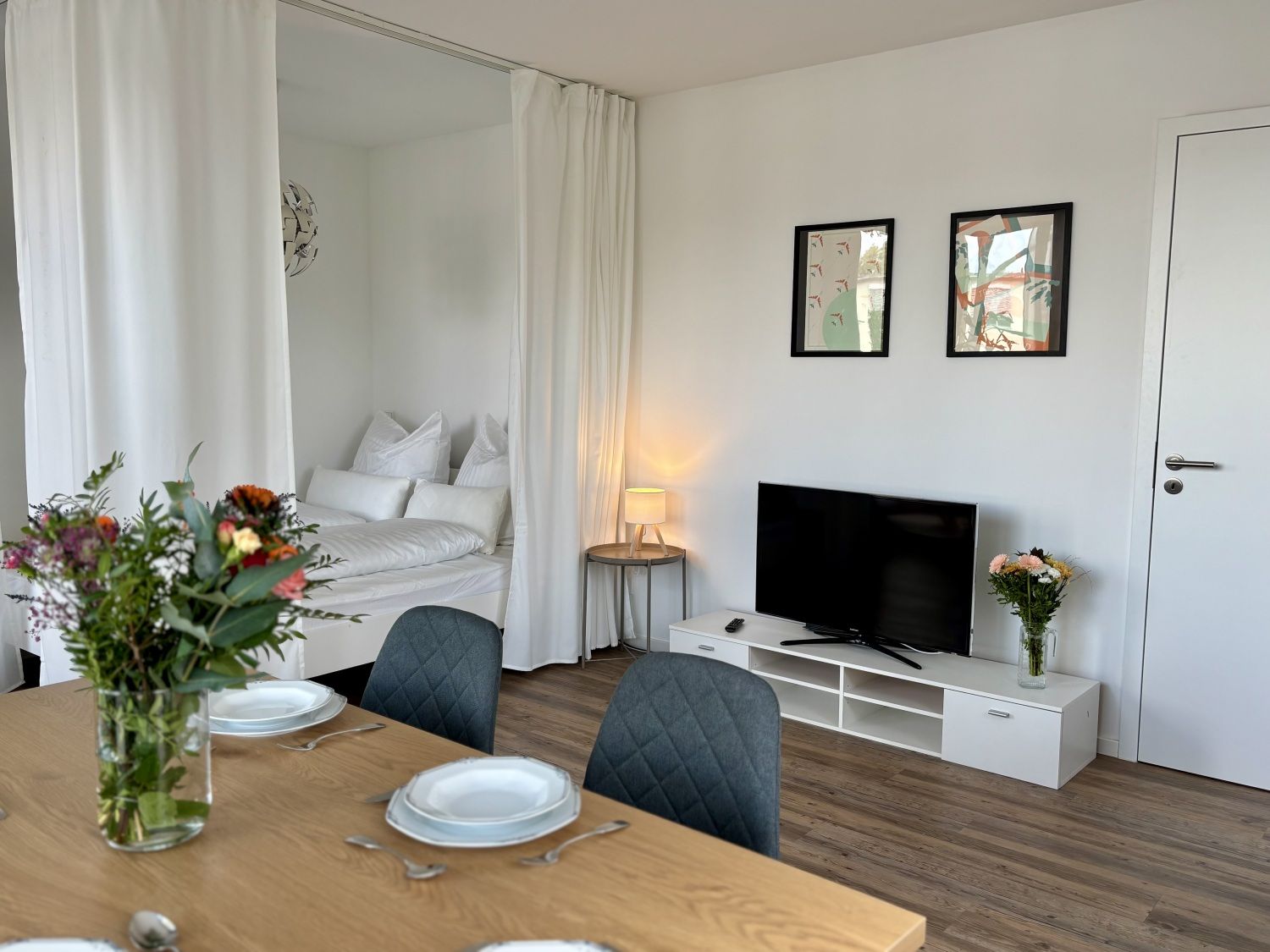 Essbereich mit Blick auf Fernseher und das Bett hinter dem Vorhang